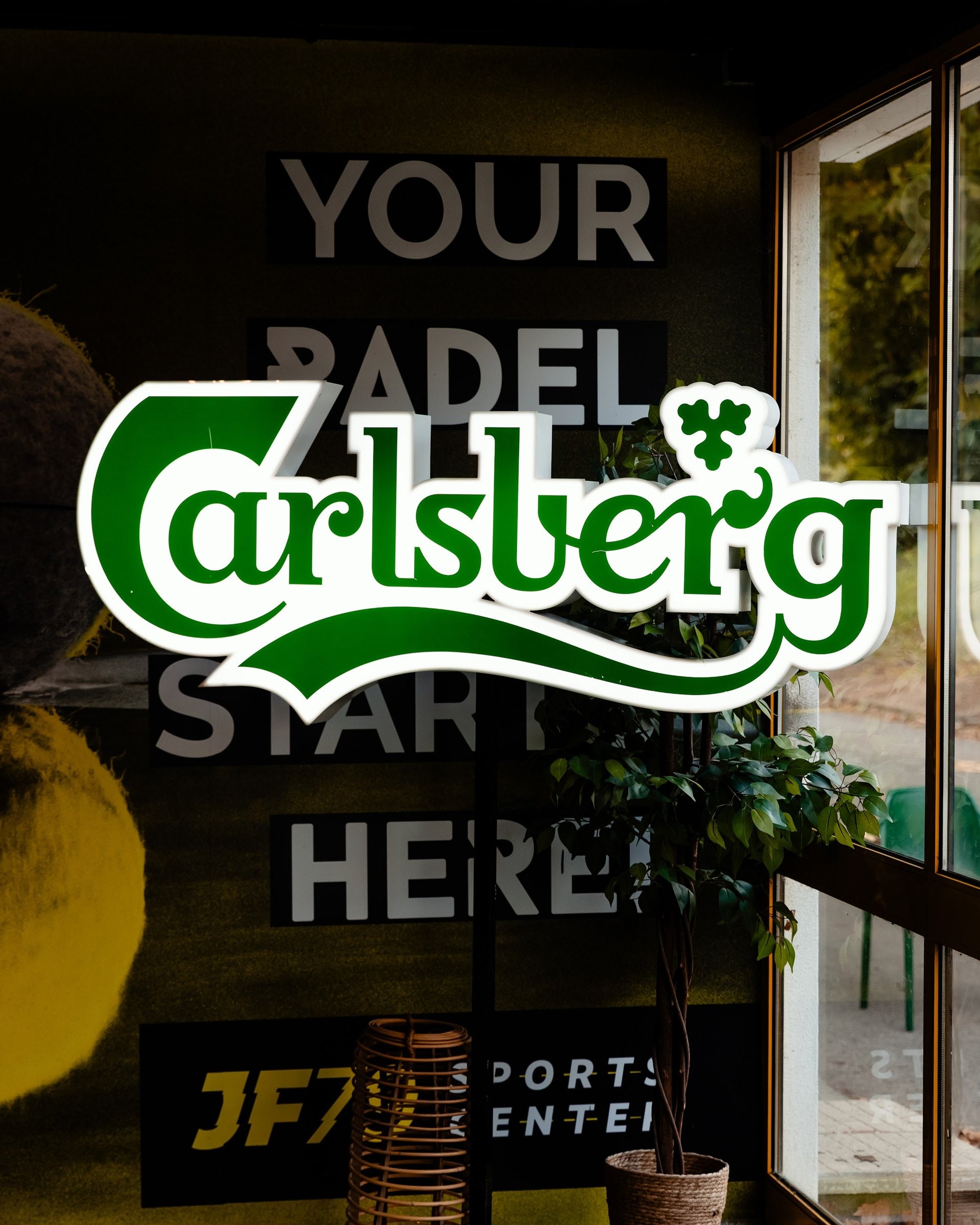 Néon da Carlsberg na entrada do clube, por cima da frase Your padel starts here