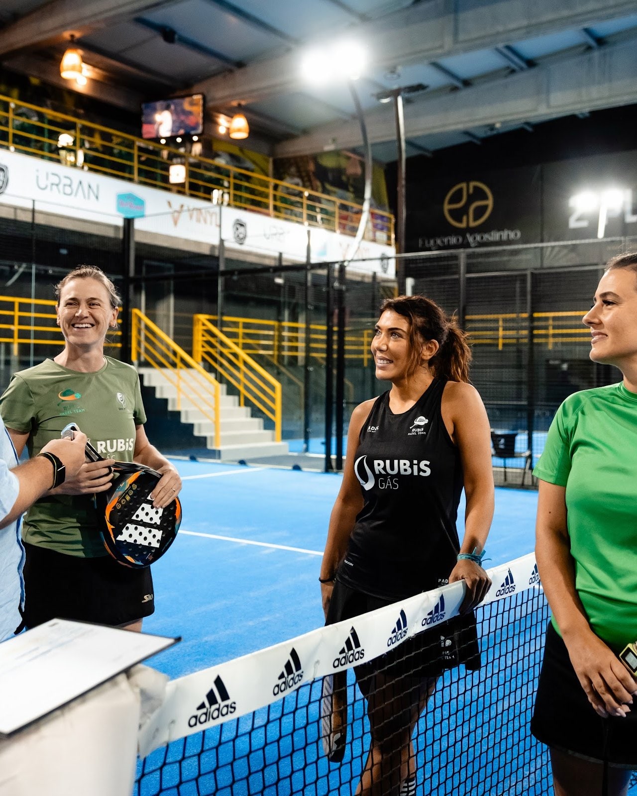 Duplas à rede antes do jogo, com a bancada amarela por trás