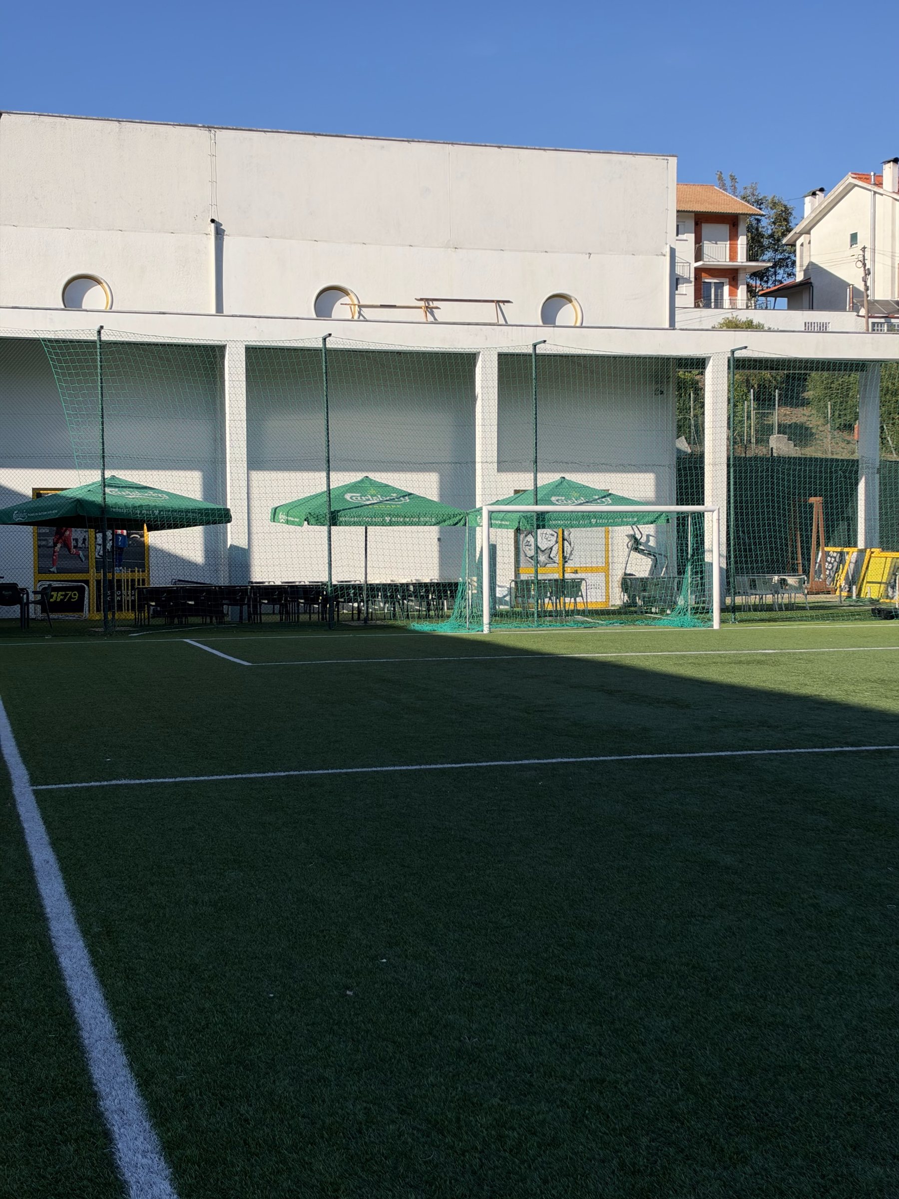 O campo de futebol de relva sintética, com as esplanadas e o pavilhão ao fundo