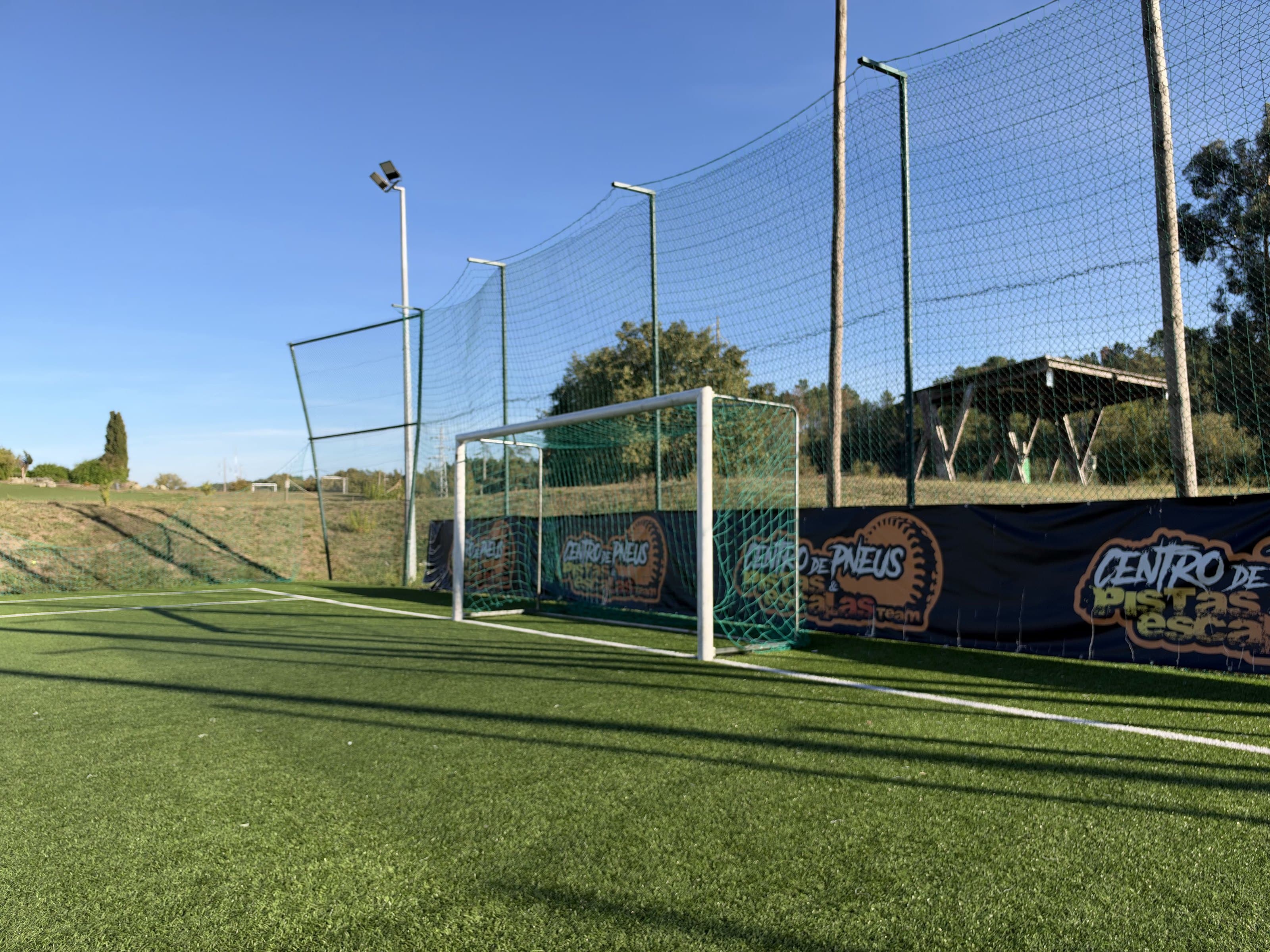 O campo de futebol de relva sintética do JF79, com a baliza e as redes de proteção ao fundo